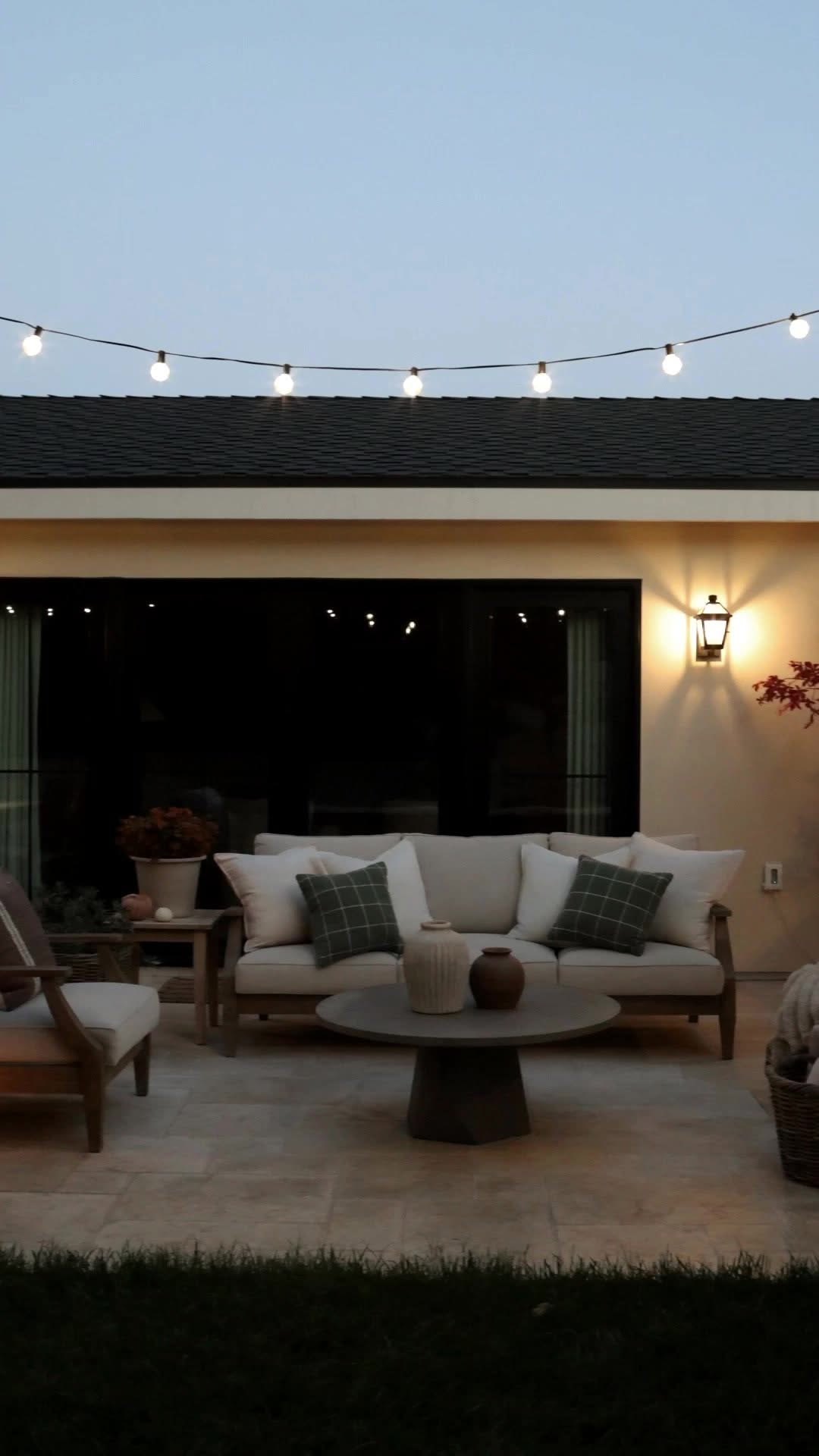 Cream outdoor sofa with plaid pillows under string lights at dusk